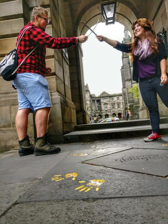 JK Rowling's handprints outside City Chambers Edinburgh, in the background a witch & wizard cross wands like pirates