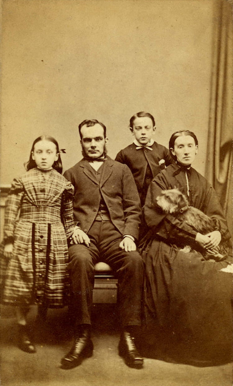 John Traill wearing a Victorian suit sits at home on Keir Street beside his wife who cradles Greyfriars Bobby